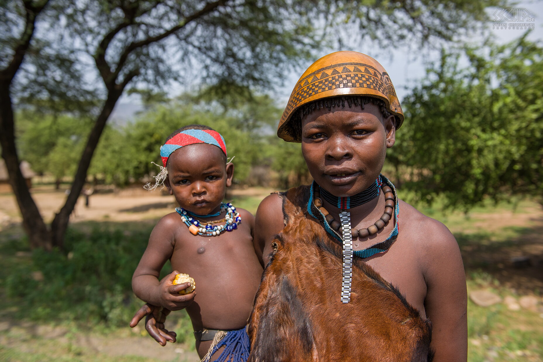 Weyto - Tsemay vrouw met kind We reden verder naar de Omo vallei, het gebied rondom de Omo rivier en het Mago NP in het zuiden van Ethiopië nabij de grenzen van Kenia en Soedan. Deze regio is het woongebied van een 20-tal etnische groepen zoals de Tsemai, Ari, Mursi, Hamer, Surma, Dassanech, Karo, Nyangatom, Banna, Arebore, ... die allen nog eigen tradities, ceremonies en unieke lichaams-versieringen kennen. Littekenpatronen, lichaamsbeschilderingen, arm- en enkelbanden, ingenieuze vlechtkapsels, kralen en lipschotels, ... het zijn allen eeuwenoude kunstzinnige uitingen. <br />
<br />
De eerste stam waarvan we een dorpje bezoeken zijn de Tsemai/Tsemay/Tsamai in de buurt van het stadje Weyto. Het zijn landbouwers en veehouders die ook bijenkorven ophangen voor honingproductie. Veel Tsemai vrouwen dragen kleding gemaakt van leder en soms ook een kalebas als hoofddeksel. Stefan Cruysberghs